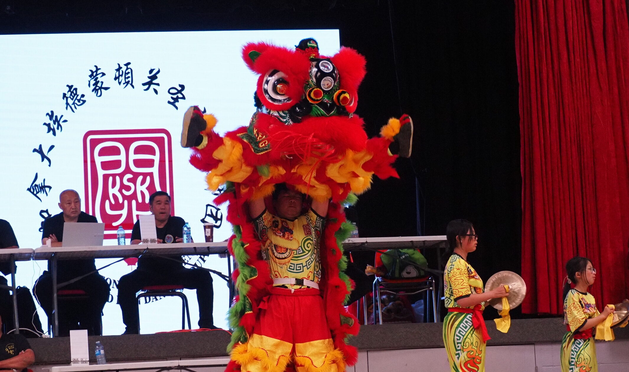 Red and green colored Chinese lion dance. Back dancer is lifting the front dancer who is doing a split kick in the air.